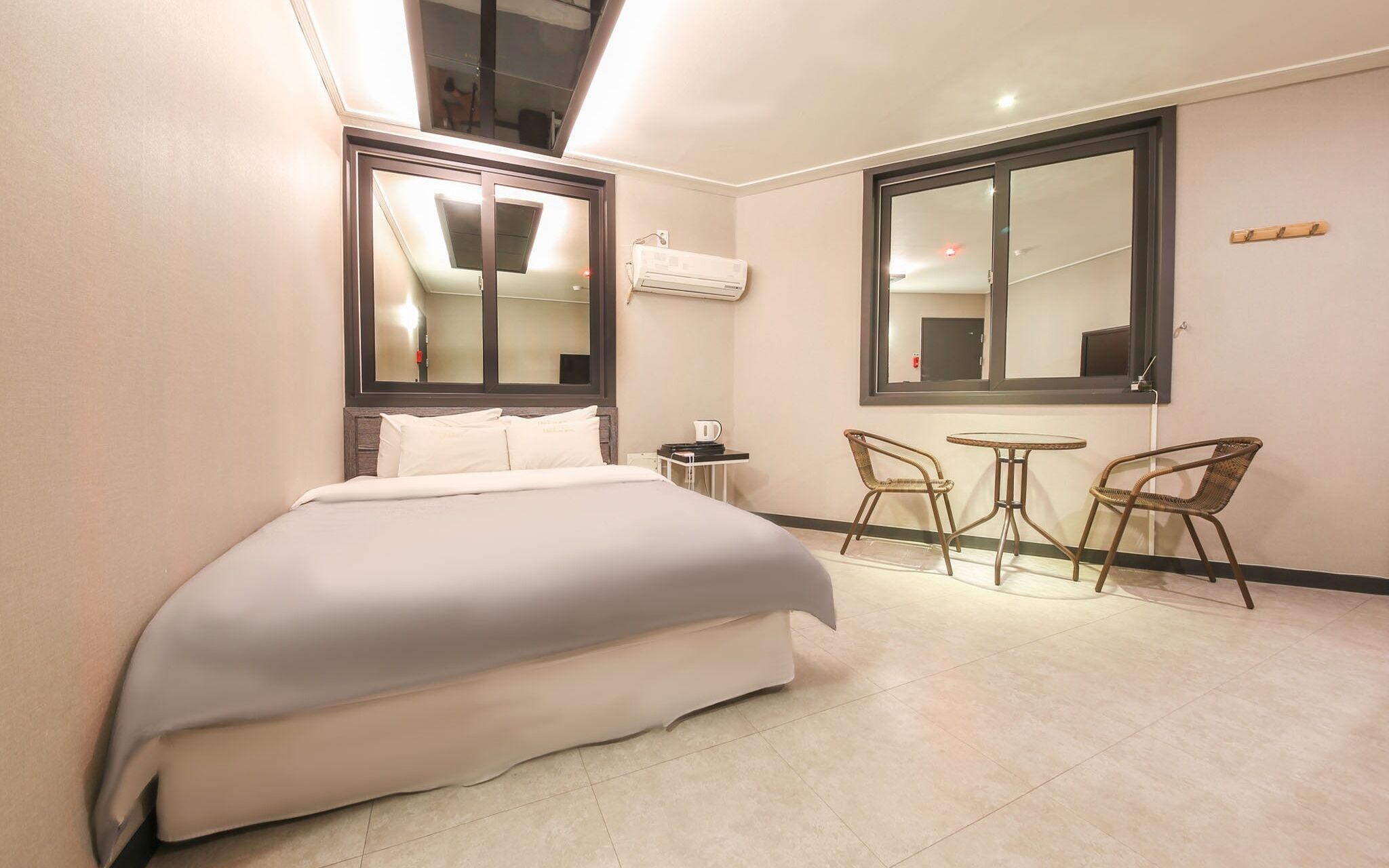 A hotel room with a bed, a small table with chairs, a large window, and an air conditioning unit.