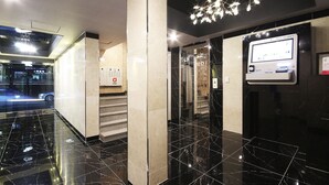 Eine moderne Hotelhalle mit Panorama-Aufzug, einem digitalen Informationsterminal und einem Marmorboden.