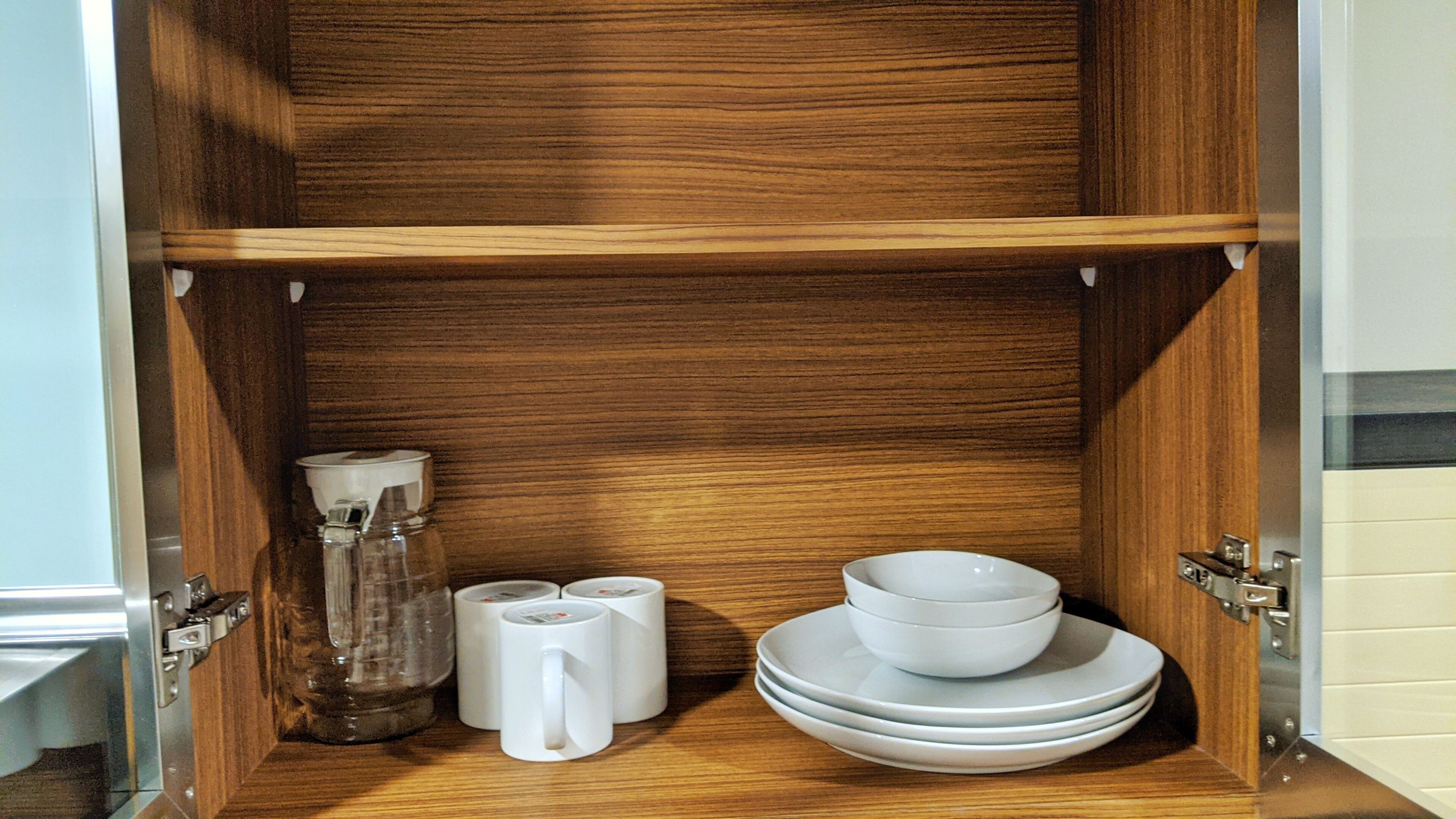 Ein Holzschrank mit einem Glasbehälter, zwei weißen Tassen und gestapelten weißen Tellern.