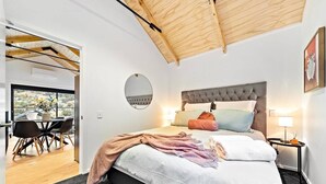 A bedroom with a large bed, a round mirror, and a dining area with chairs and a table. - 4 Bedroom, Brand New, Modern Mountain View Paradise (Queenstown)