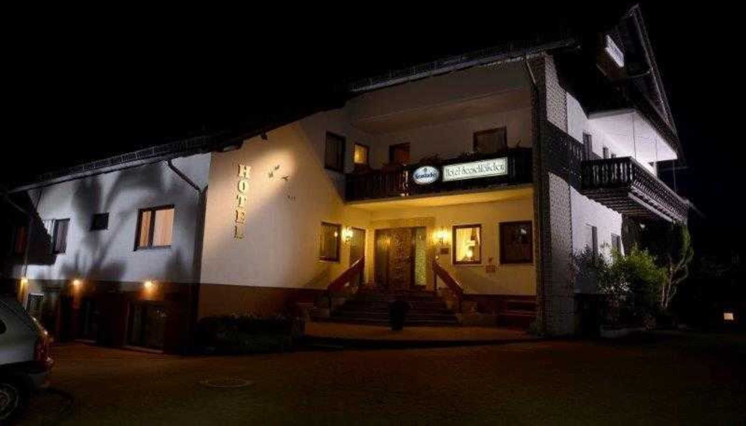 A hotel with a sign 'HOTEL' above the entrance, a staircase leading to the main door, and a balcony on the upper floor.