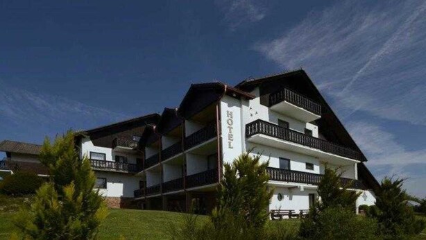 Un hotel de varios pisos con balcones, cielo despejado y vegetación en primer plano.