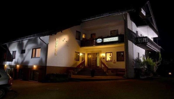 A hotel with a sign 'HOTEL' above the entrance, a staircase leading to the main door, and a balcony on the upper floor.