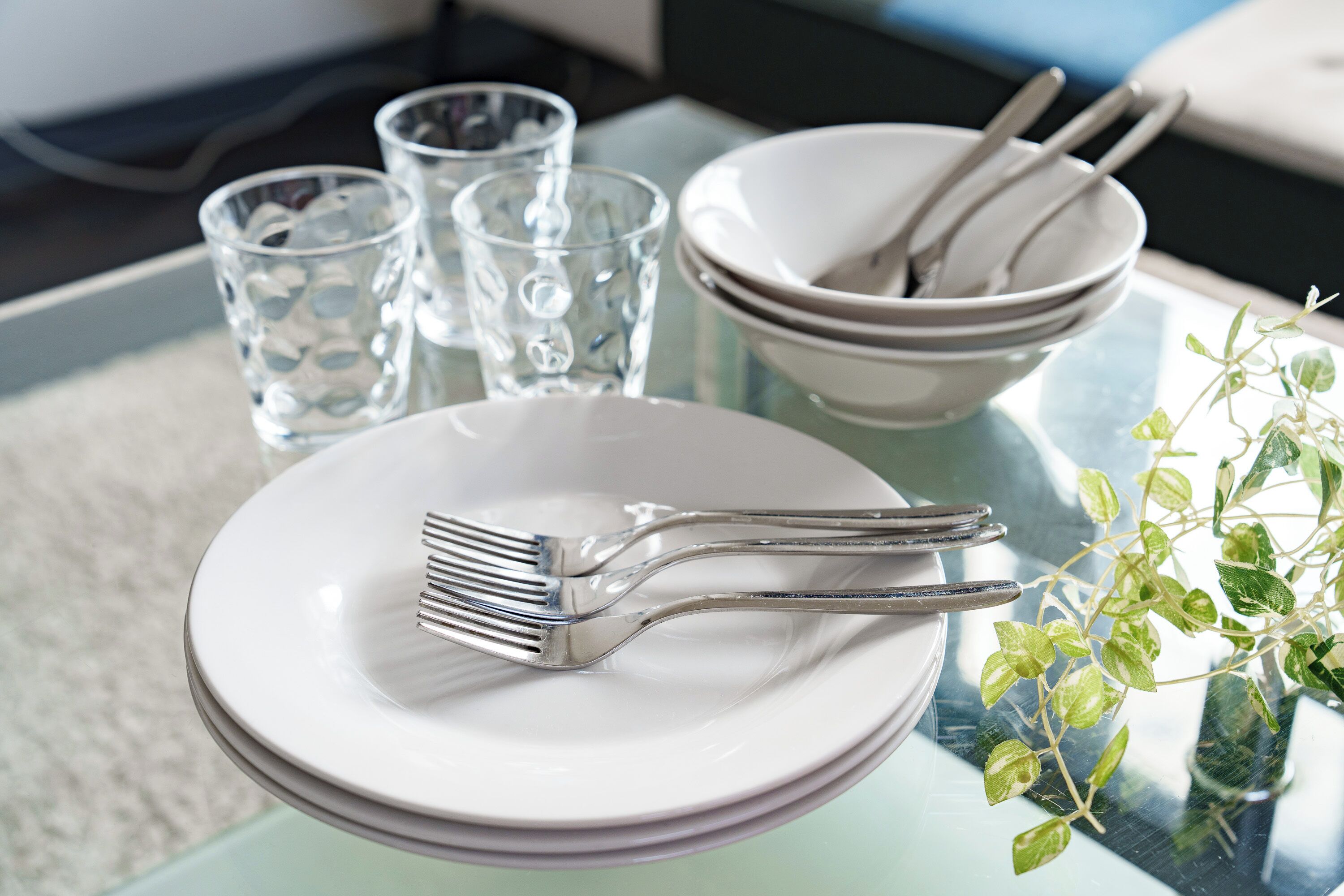 A dining table with stacked white plates, a fork, a bowl, and two glasses.