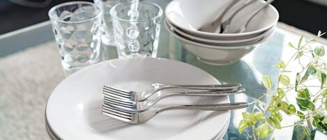 A dining table with stacked white plates, a fork, a bowl, and two glasses.