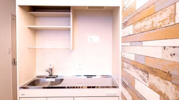 A compact kitchen with a stainless steel sink, white cabinets, and a wooden accent wall.