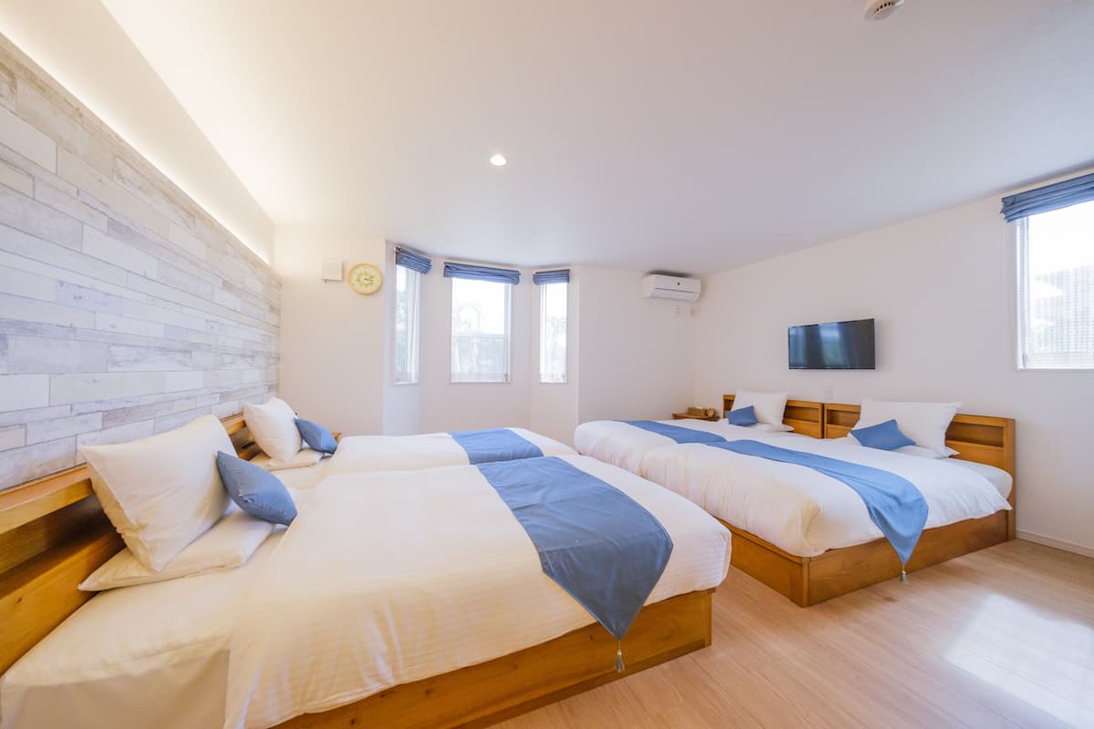 A room with two beds, a wooden headboard, a flat-screen TV, and a window with curtains.