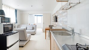 A modern kitchen with a built-in microwave, a sink, and a stove. There is a dining area with a table and chairs. - ecot Irabu Bridge Premier (Miyakojima)