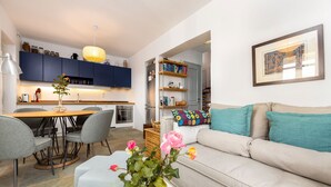 A modern living room with a sofa, a dining table, and chairs. There is a kitchen area with cabinets and a stove. - Bralos Villa - Paros - Near Naousa, spectacular sea views, 2 bedrooms, privacy (Paros)