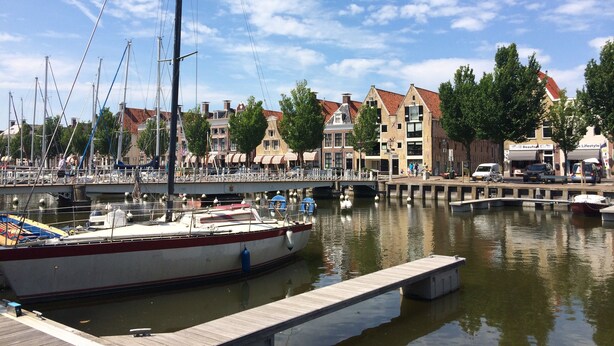 Un port de plaisance avec des bateaux amarrés, une jetée en bois et, au fond, des bâtiments à l’architecture traditionnelle.
