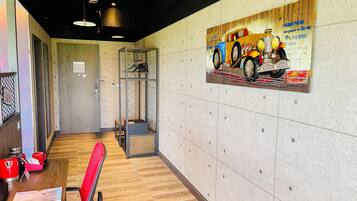 A modern office space with a wooden floor, a red chair, a table with a red kettle, and a wall-mounted artwork of a vintage car.