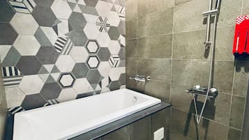 Een moderne badkamer met een backsplash van geometrische tegels, een witte badkuip en een douche met een handdouche.