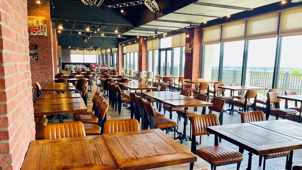 A spacious restaurant with long wooden tables and leather chairs, large windows offering a view, and a brick wall on one side. - Lihpao Resort - T11T12 Hotel (Taichung)