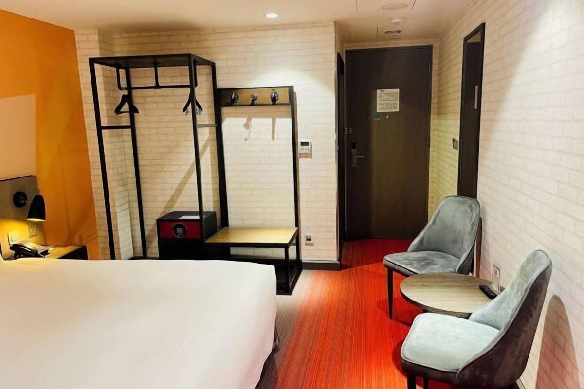 A hotel room with a bed, a desk, a chair, a bench, and a wardrobe.