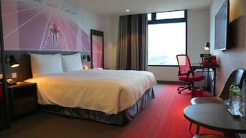 A hotel room with a bed, a desk, a chair, a window, and a wall with a sports-themed poster.