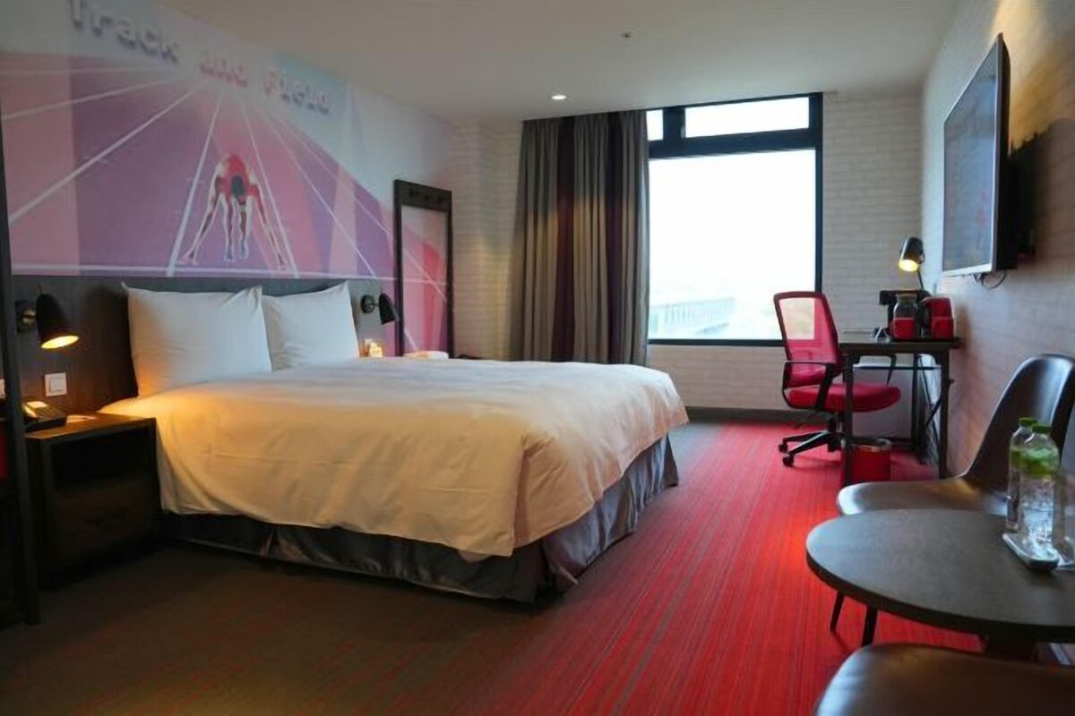 Una habitación de hotel con una cama, un escritorio, una silla, un televisor y un ventanal grande.