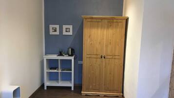 A small room with a wooden wardrobe, a white shelf unit, and two framed pictures on the wall.