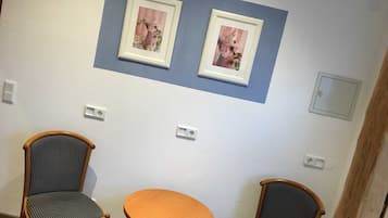 Ein Zimmer mit zwei gerahmten Bildern an der Wand, zwei Holzstühlen mit gestreiften Kissen und einem kleinen Holztisch sowie Steckdosen.