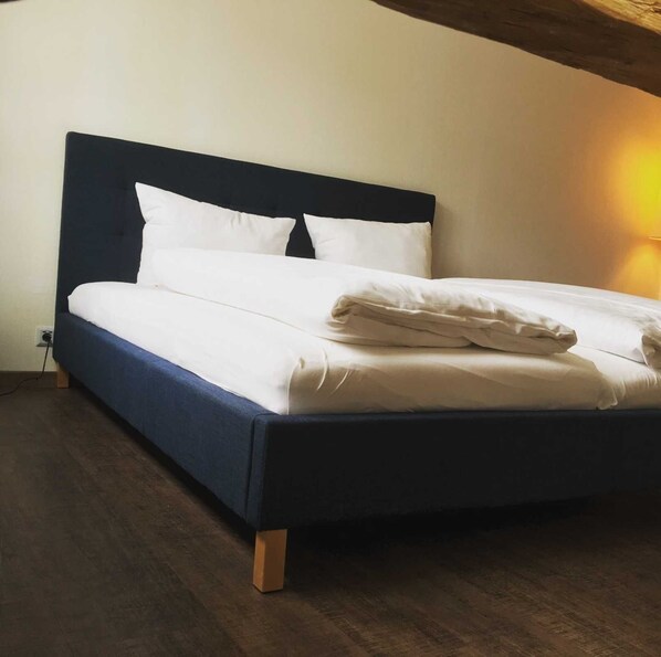 Un lit avec une tête de lit sombre, du linge de lit blanc et un plancher en bois.