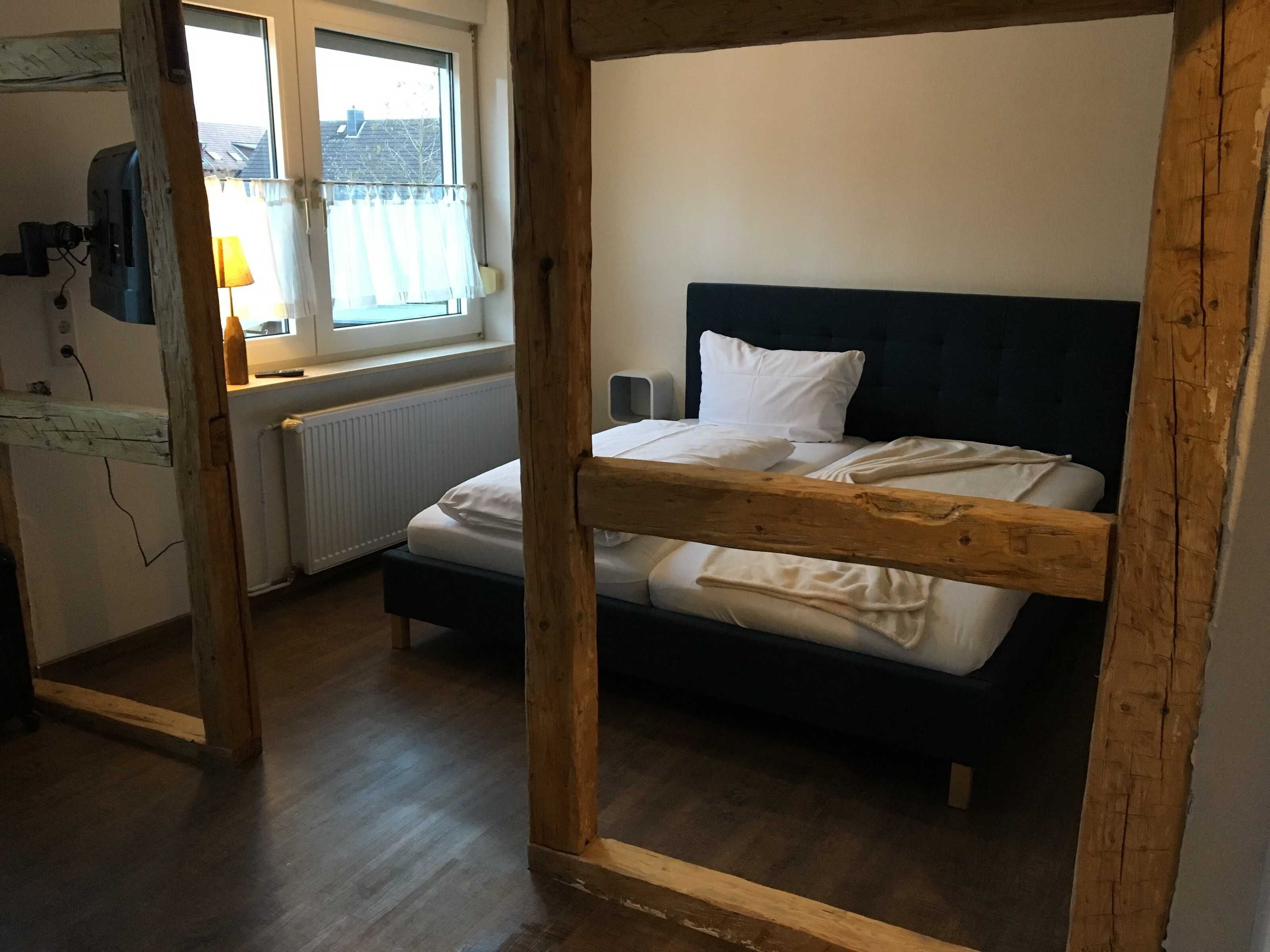 A room with a bunk bed, a window with curtains, a radiator, and a lamp.