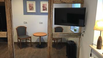 Une chambre d’hôtel avec un téléviseur à écran encadré de bois, deux chaises, une petite table ronde et une lampe.