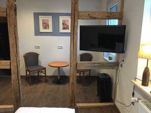 Une chambre d’hôtel avec un téléviseur à écran encadré de bois, deux chaises, une petite table ronde et une lampe.
