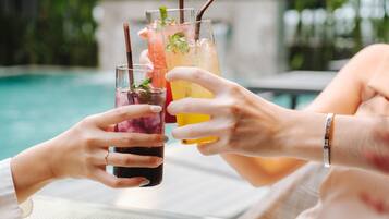 Two people holding glasses of iced drinks by a pool.