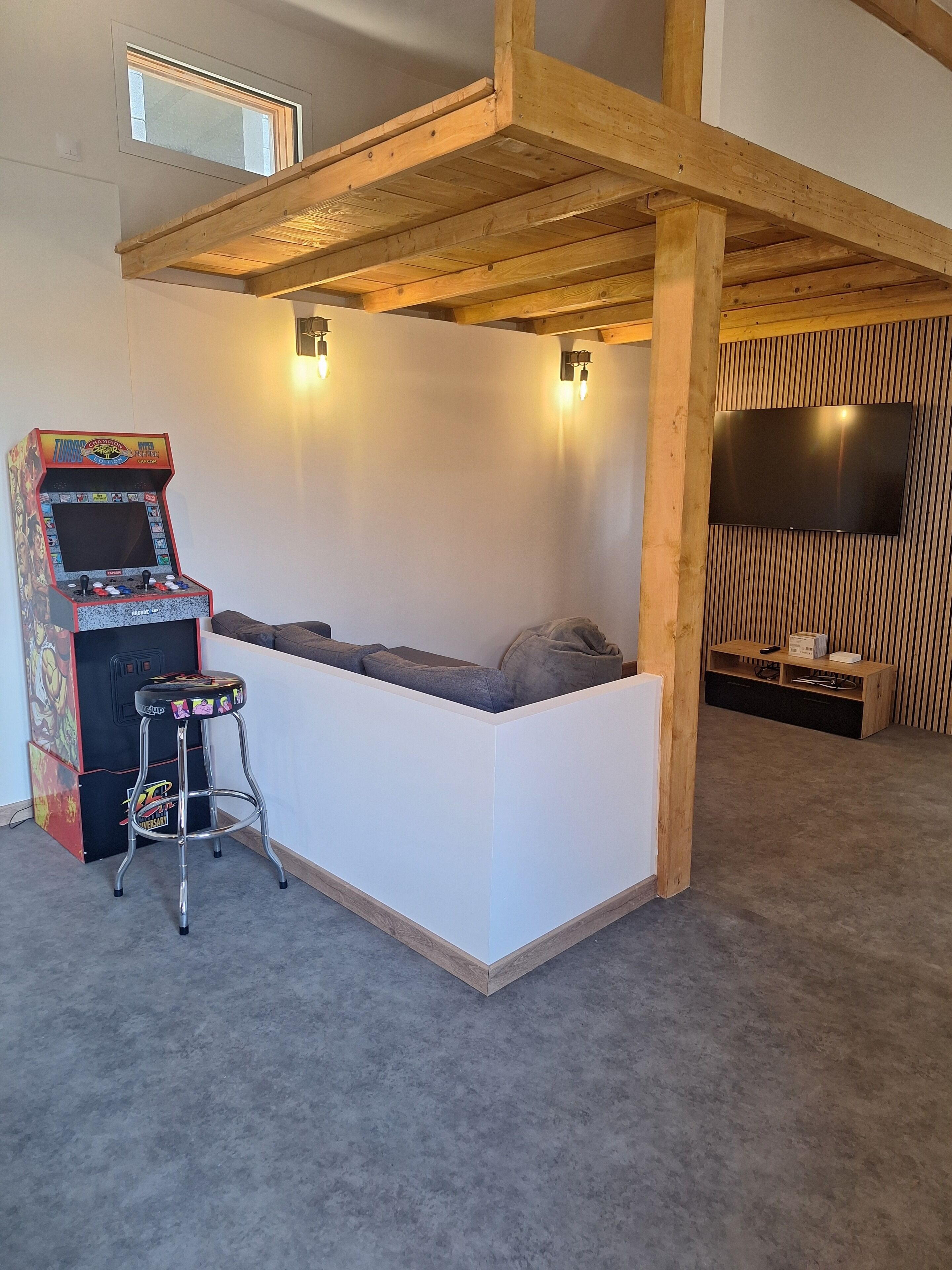 A cozy room with a built-in seating area, a ceiling-mounted TV, and a retro arcade machine.