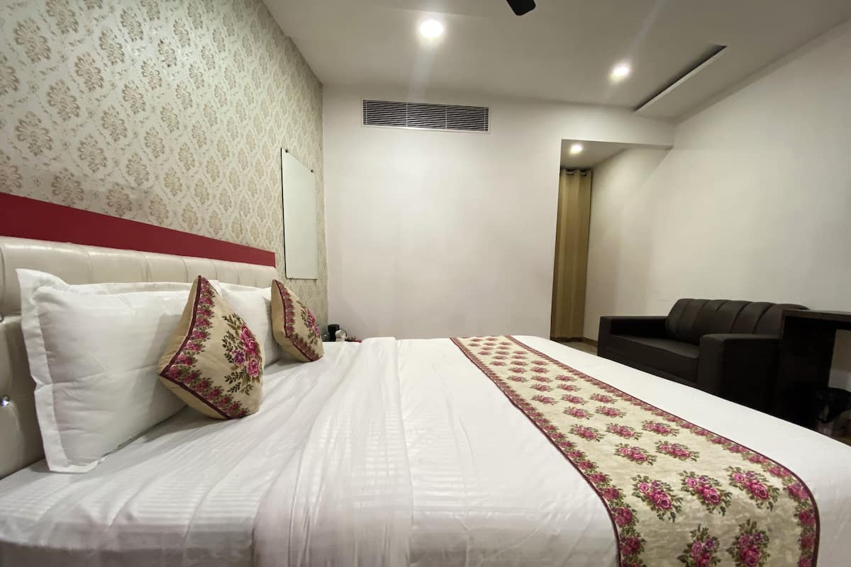 A neatly made bed with white bedding and floral-patterned pillows, a dark brown sofa, and a patterned wall.