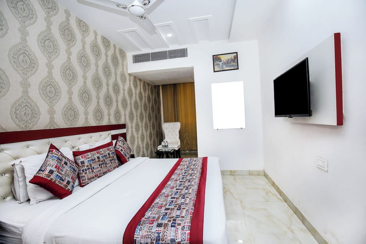 A hotel room with a large bed, a TV mounted on the wall, and a patterned wallpaper.