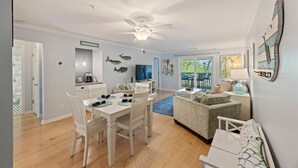 Ein geräumiges Wohnzimmer mit Esstisch, weißen Stühlen, einer Couch und einem Deckenventilator.