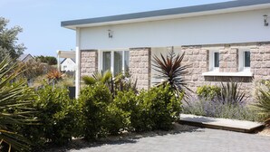 A modern house with a stone facade, large windows, and a well-maintained garden with various plants. - Villa Espérance, a stone's throw from Barneville beach, rated 3 ***. (Saint-Jean-de-la-Rivière)