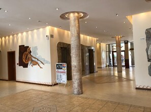 A spacious lobby with a central column, a mural of a warrior, and an ATM sign. - Aparthotel Poseidon - All inclusive (Sunny Beach)