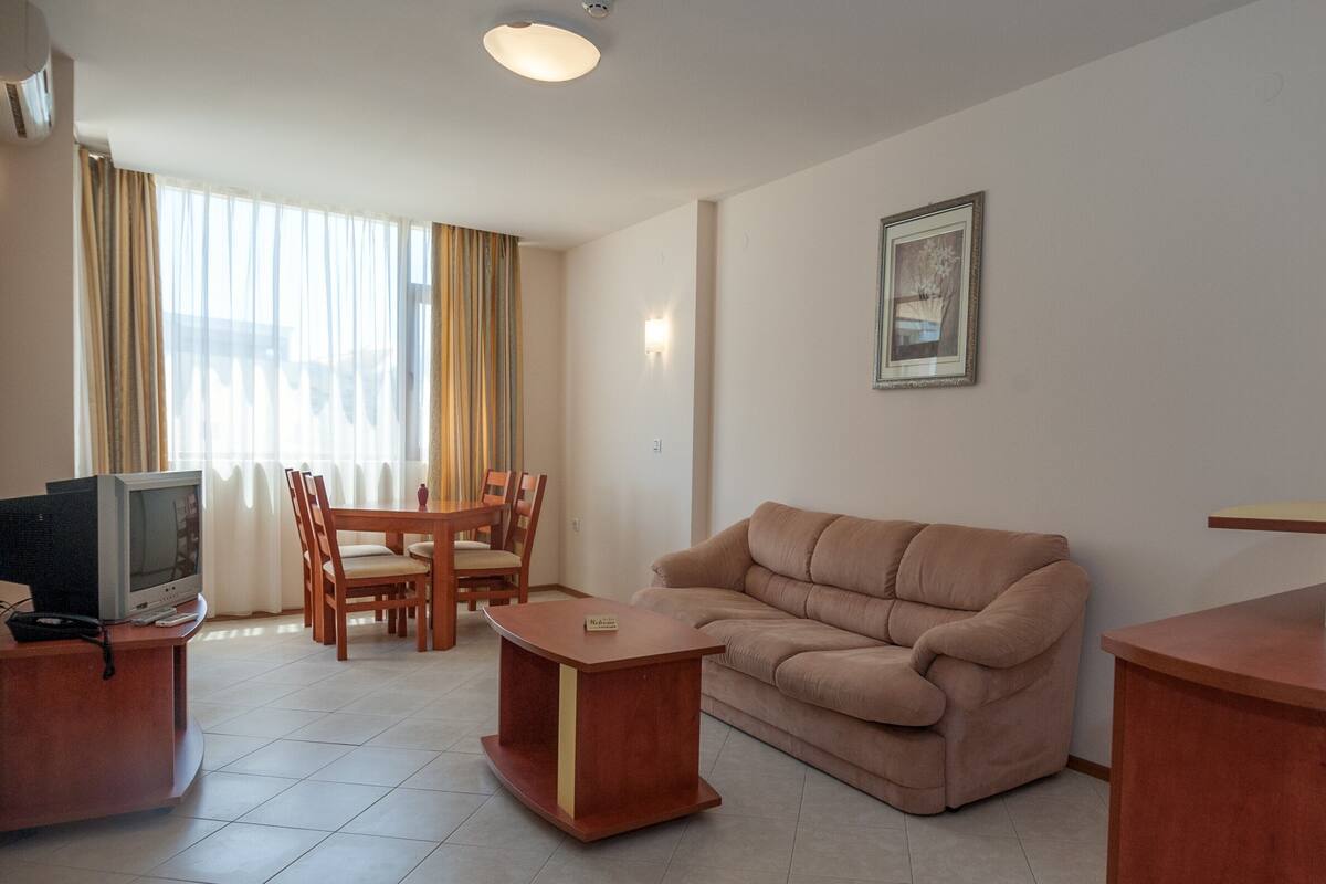 A living room with a sofa, a coffee table, a TV, and a dining area with chairs and a table.