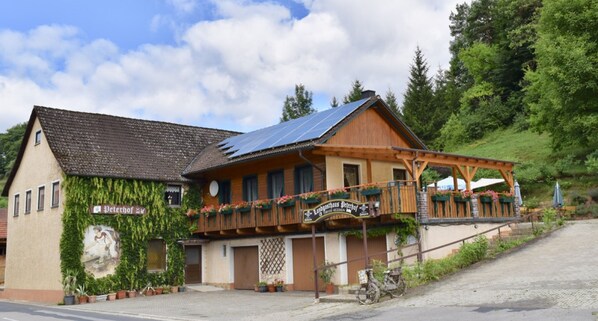 Un bâtiment traditionnel en bois, doté d’un toit en pente, d’un balcon orné de jardinières et d’une enseigne indiquant qu’il s’agit d’un restaurant.