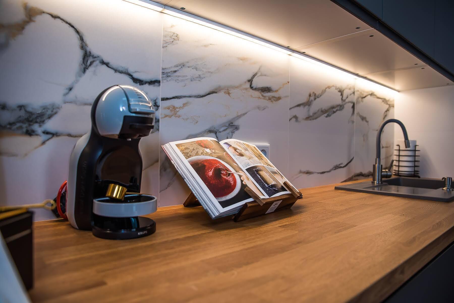 A kitchen with a marble backsplash, a coffee machine, a magazine, and a modern faucet.