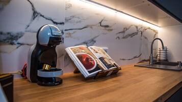 A kitchen with a marble backsplash, a coffee machine, a magazine, and a modern faucet.