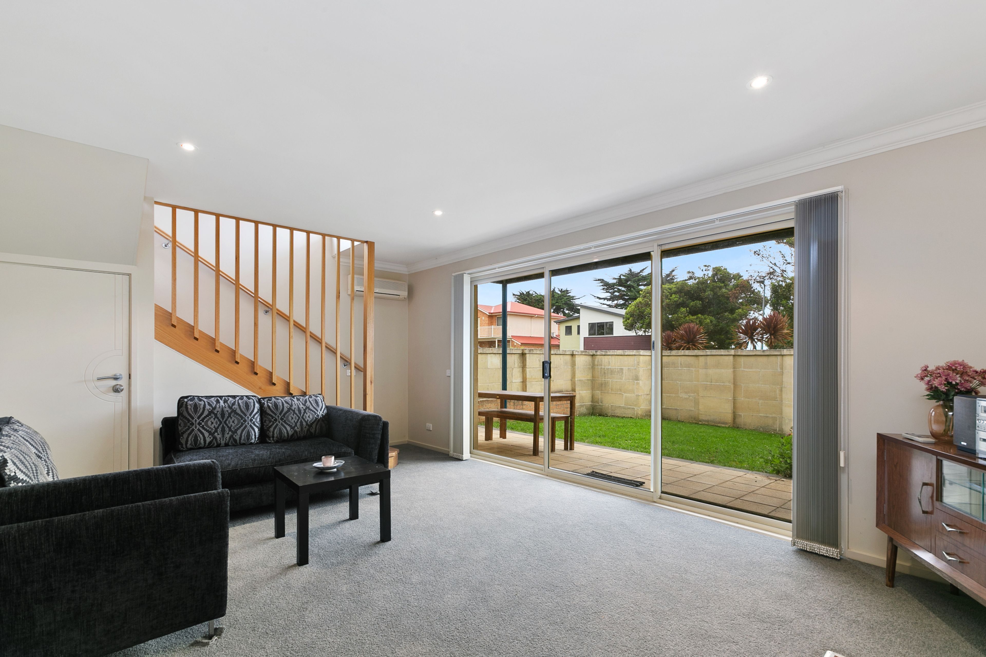 A spacious living room with a staircase, a sofa, a coffee table, and a sliding glass door leading to a backyard.
