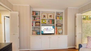 Ein Zimmer mit einem eingebauten Bücherregal, einem Fernseher und einem gemusterten Teppich.