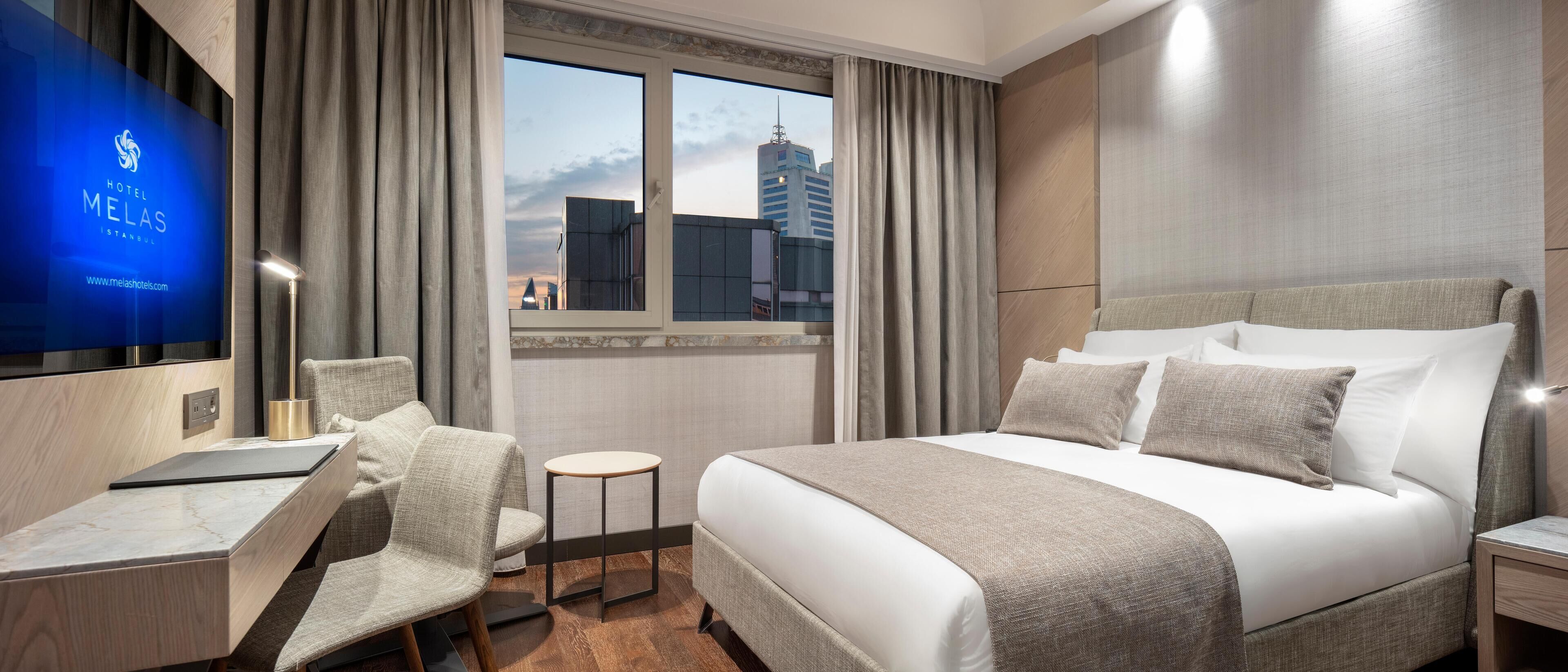 Habitación de hotel con cama, escritorio, silla, mesita pequeña y televisor.
