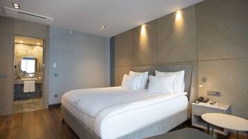 Una habitación de hotel moderna con una cama grande, una mesita de noche con teléfono y lámpara, y una pequeña mesa redonda.