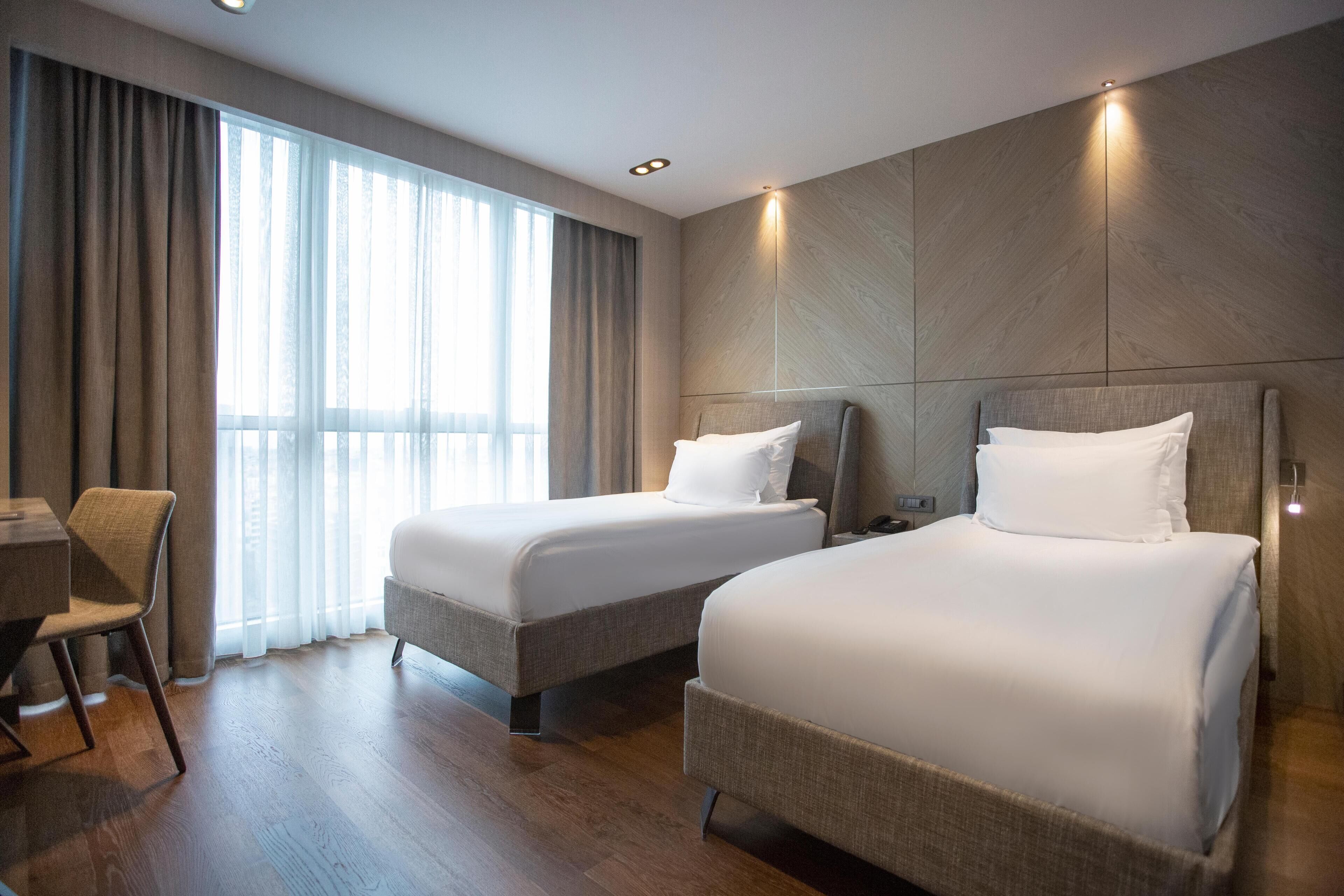 A hotel room with two beds, a desk, and a chair.
