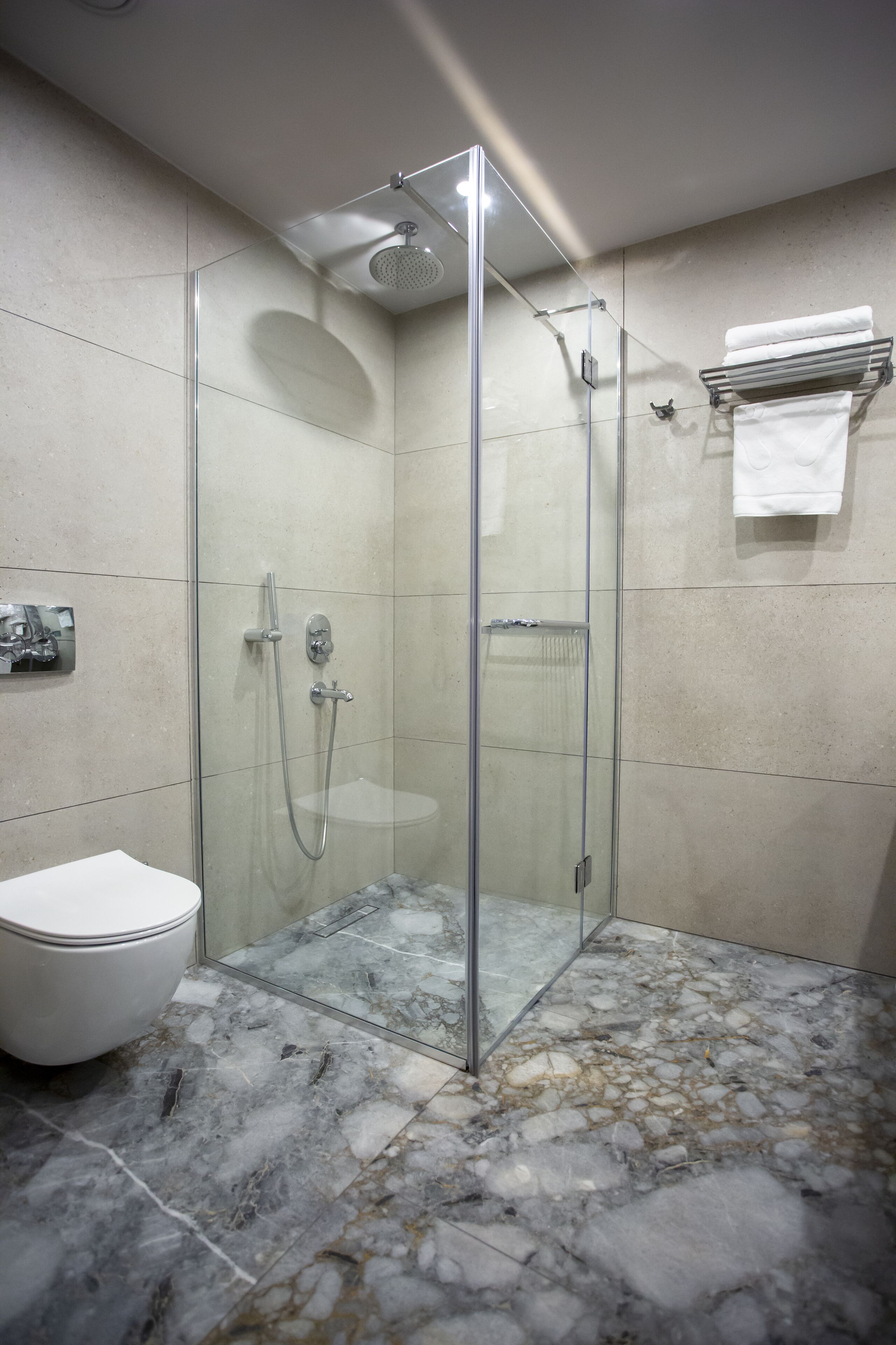 A modern bathroom with a glass-enclosed shower, a white toilet, and a marble floor.