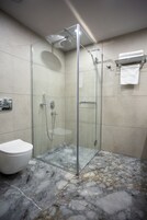 Un baño moderno con cabina de ducha de vidrio, un inodoro blanco y suelo de mármol.