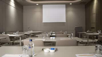Un salón de conferencias con mesas, sillas, botellas de agua y una pantalla de proyector.