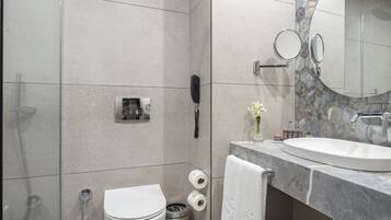 Un baño moderno con lavamanos de mármol, cabina de ducha de vidrio, inodoro y tocador con espejo.