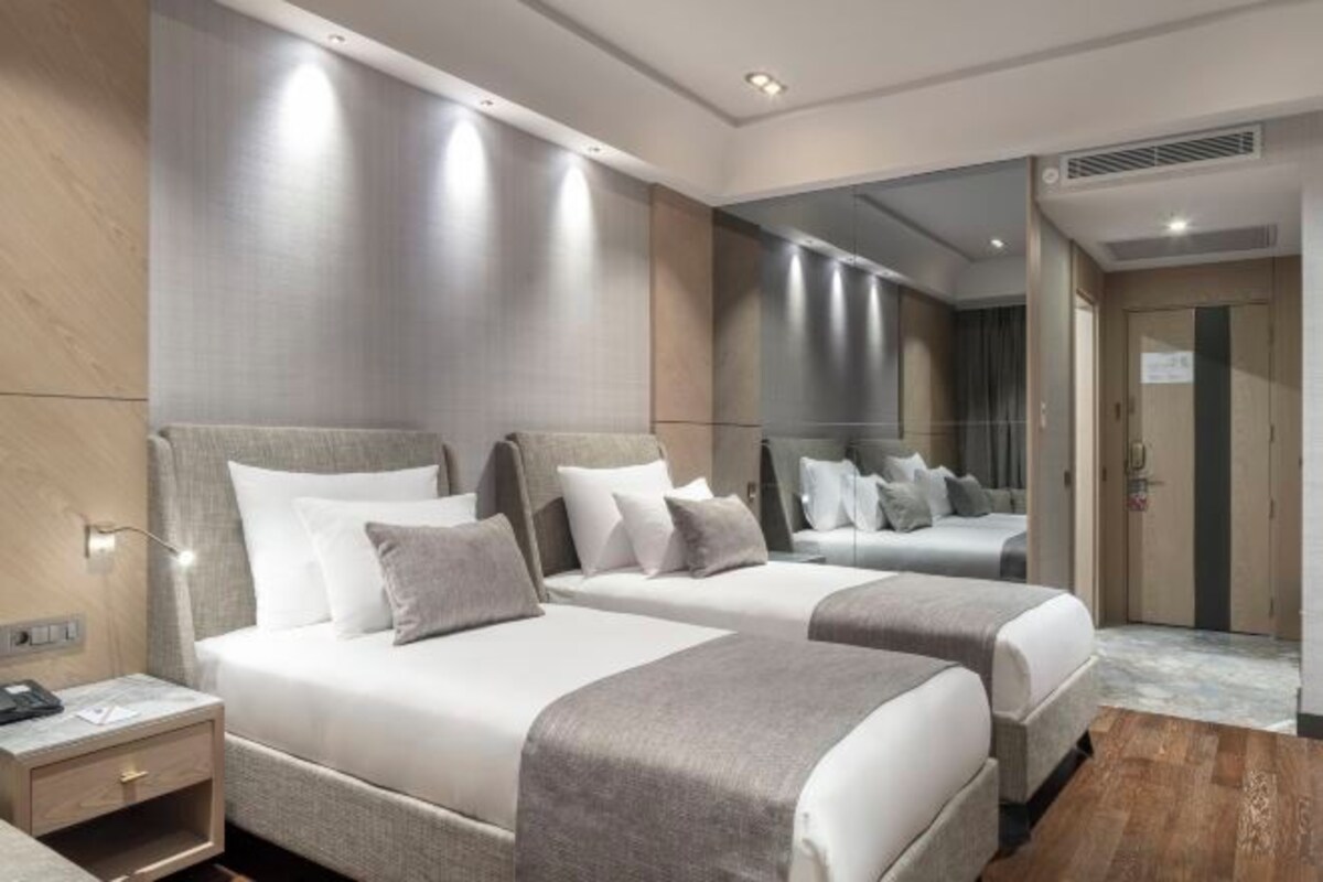 A hotel room with two beds, a nightstand, a mirror, and a door.