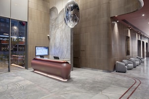 Un área de recepción moderna con un mostrador curvo, una gran escultura fijada a la pared y una fila de asientos a lo largo de la pared.
