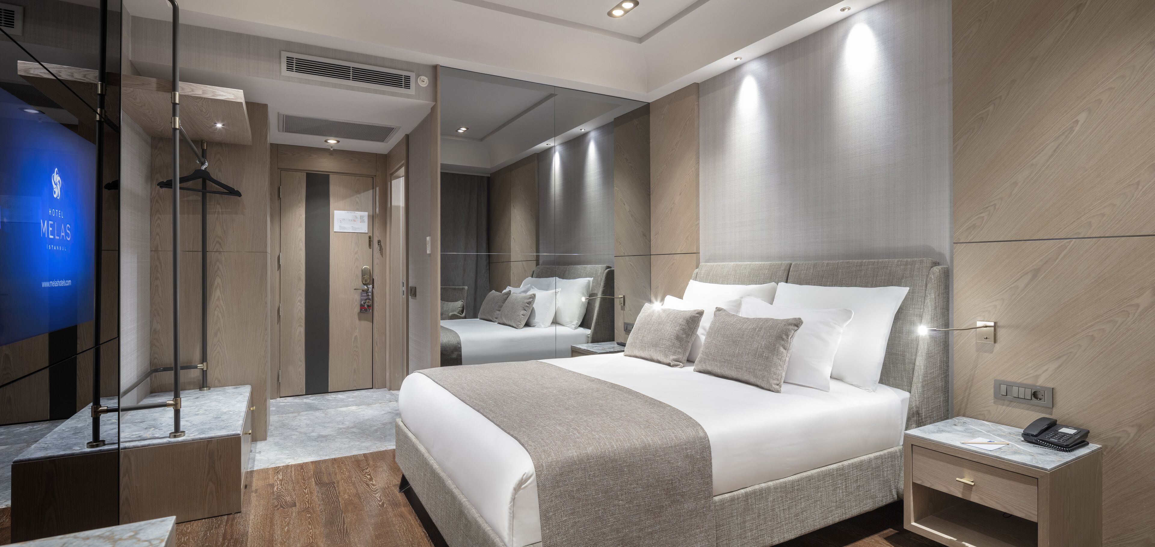 A modern hotel room with a large bed, a bedside table with a phone, and a TV in the corner.