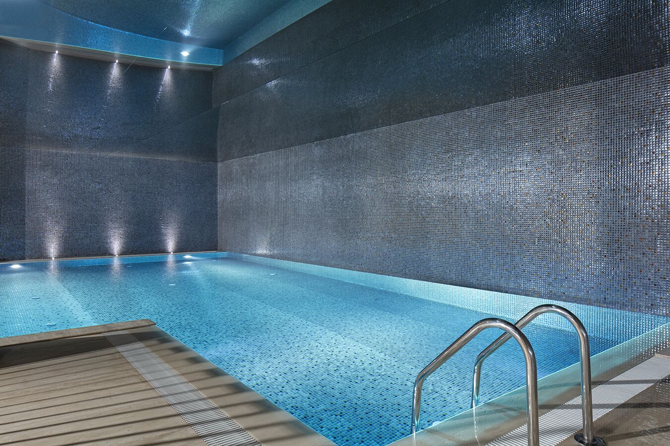 Una piscina con un muro de azulejos y una zona de cubierta de madera.
